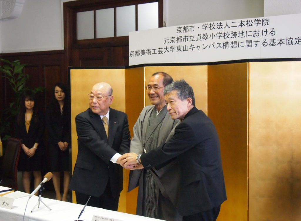締結式で握手を交わす門川大作市長（中央）と京都美術工芸大の新谷秀一理事長（左）、河野元昭学長(右)　提供：京都市