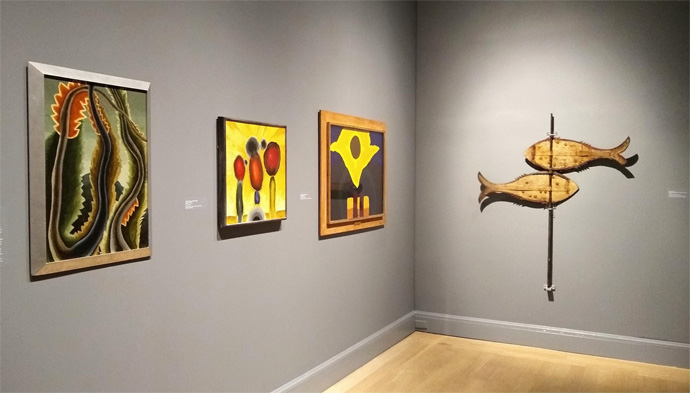 「イーデス・ハルパートとアメリカ美術の台頭」展の展示風景。右の壁は《魚の形の風向計》19世紀後期、左の壁はアーサー・ダヴの絵画：左から《木の形》1932年、《夜明けIII》1932年、《真昼》1944年。筆写撮影