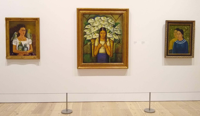 「Vida Americana（American Life）―メキシコ壁画がアメリカ美術を変えた 1925-1945年」展の展示風景。左より：フリーダ・カルロの自画像《私と私の鸚鵡》1941年、アルフレド・ラモス・マルティネス《カラー売り》1929年、フリーダ・カルロ《二人の女》1929年　筆者撮影