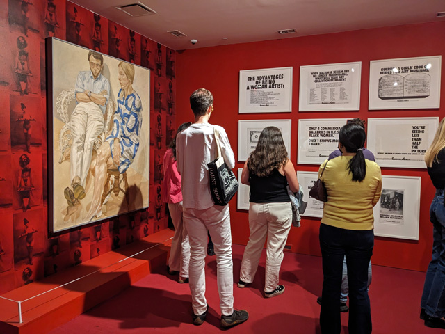 最初の部屋の展示風景。左：フェミニズム美術史の始祖的存在のリンダ・ノクリンと夫のフィリップ・ポマーの肖像はフィリップ・パールスタインの作品、1968年　右：アートにおける男女の不均衡を弾劾するゲリラ・ガールズのポスター作品。ともにブルックリン美術館蔵