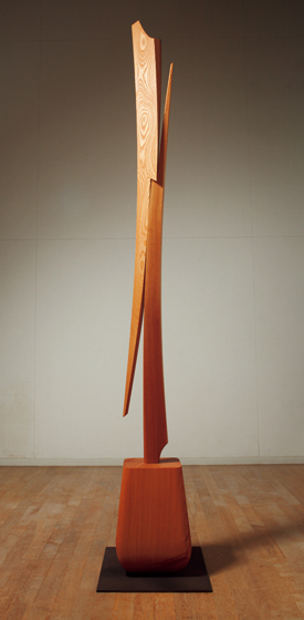 欅材で断面が二等辺三角形の長材を使い、二本の「そりのあるかたち」を削り出し、一点で交互に重ね接ぎした単純な構成で、緊張した木の美しさを表現したかった。<br />
台座は、松の角材を壺状に削り込んだ形に仕上げ、上部の細身の「そりのあるかたち」の力を受けさせている。