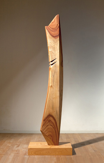 「そりのあるかたち」は平櫛田中賞を受賞した頃より本格的に作品タイトルとし始めた。木、石、ステンレスなどを素材に制作を続け、今回は50年ほどアトリエに寝かせていた樟を使った。刀でいう刃と背の部分の峰、鎬（しのぎ）を含む６面で構成し、切込みを入れアクセントとした。木は削って初めて表情が現れる楽しさがある。本作はその表情と「そりのあるかたち」が一体となるよう祈った。