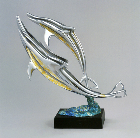 バハマ諸島の中のビミニ島という小さな島でイルカとの出合いを待った。初めてのスキューバダイビングをしながらの、海中での出合いである。数日が過ぎ、やっとすばらしいときめきの瞬間がきた。彼らと遊ぶこと約20分。その時の感動をアルミニューム、金箔、銀箔を使い制作した。