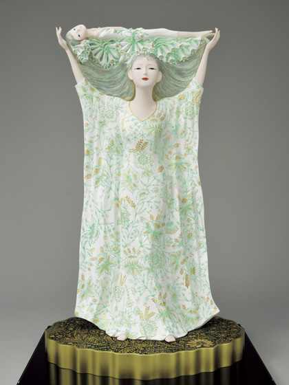 東日本大震災は多くの尊い命と、かけがえのない愛や絆も一瞬におし流してしまいました。原発の不安に怯えるなか、蘇れいのちと叫ぶ思いを、幼子を頭上にいだきあげて、天に命を希い生きて生きてと叫び続ける姿を、濁流から離れ清められた白い衣装をつけて表現しました。台座は静かに波うつ海を思い制作しました。